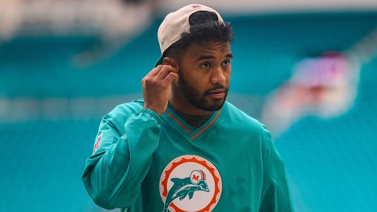Miami Dolphins player in teal jacket adjusting earpiece.
